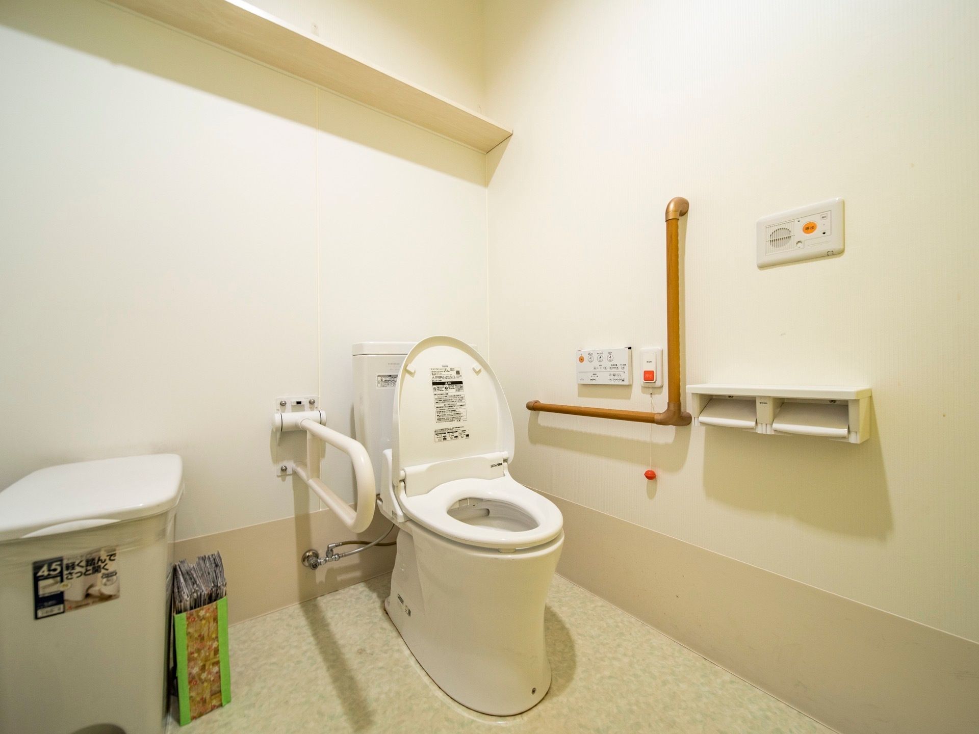 ふたつき便座のトイレが設置されている。洗浄暖房機能の操作パネルの横に、手すりや緊急呼び出しボタンがついている。