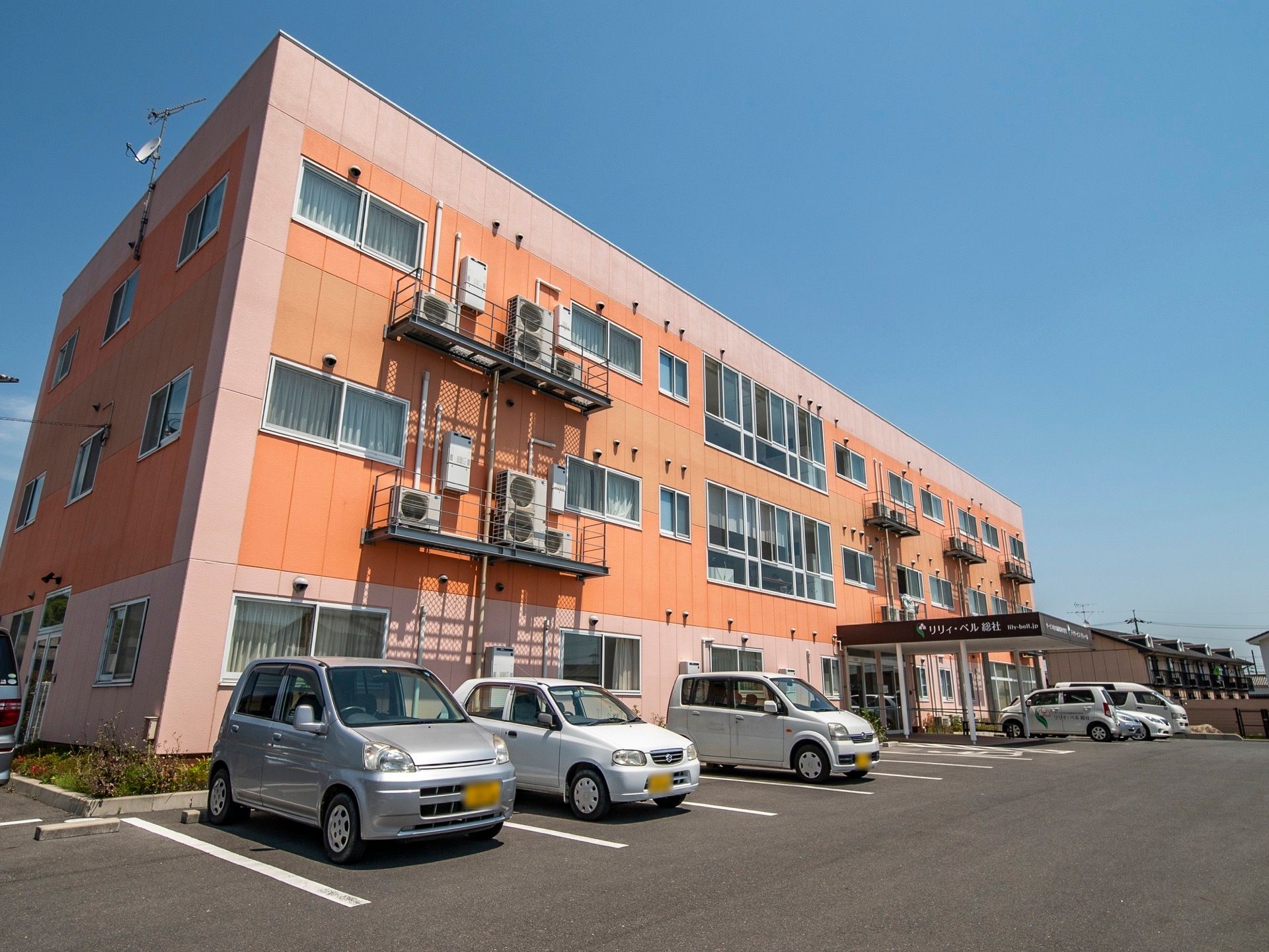 ピンク色やオレンジ色を基調としたカラフルな外壁の３階建ての施設である。玄関前には大きなひさしがある。