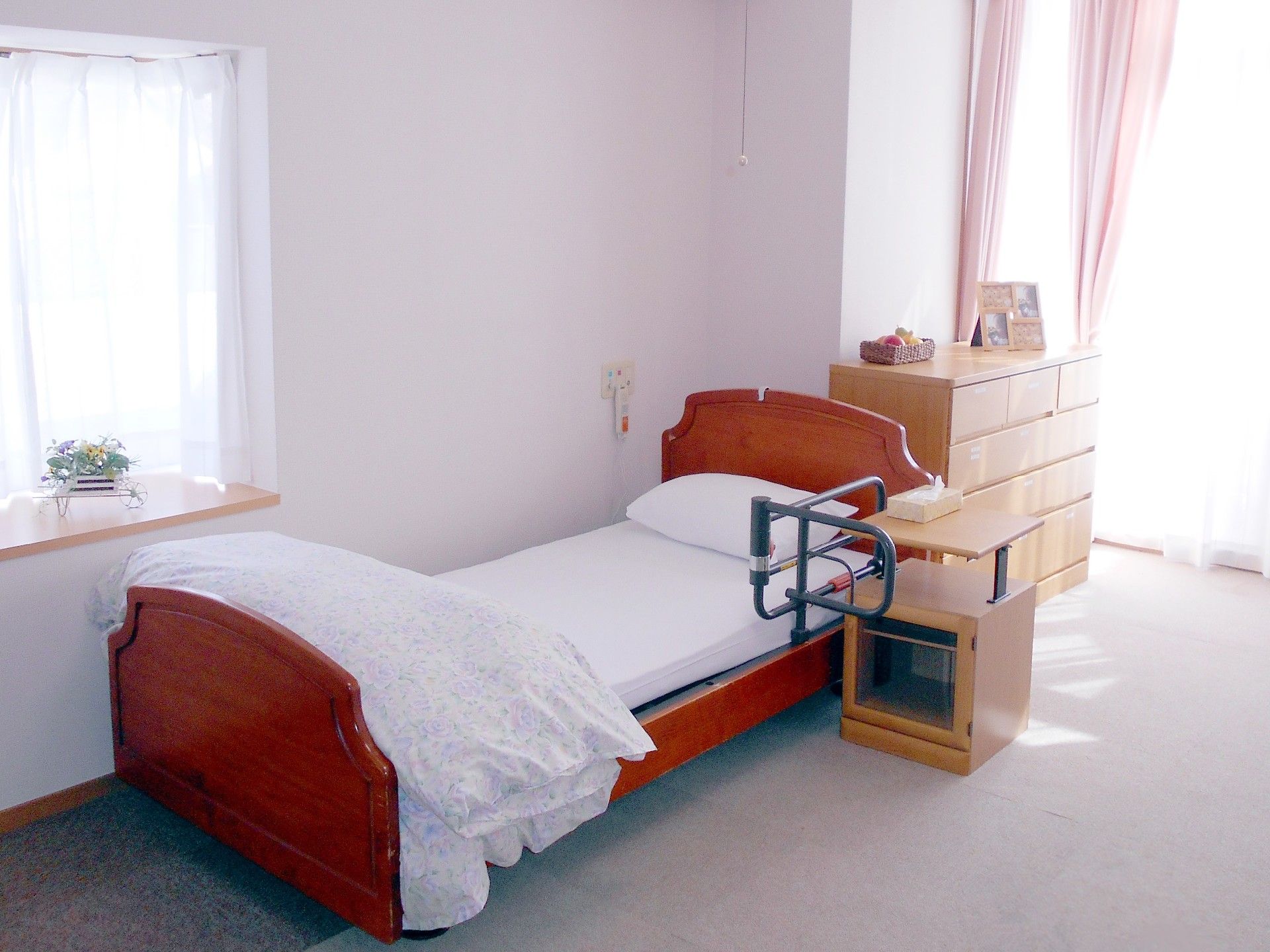 部屋には、キャビネットやサイドテーブルを配置して、住みやすい環境にできる。ベッドに黒い柵を設置して、転倒防止対策をしている。