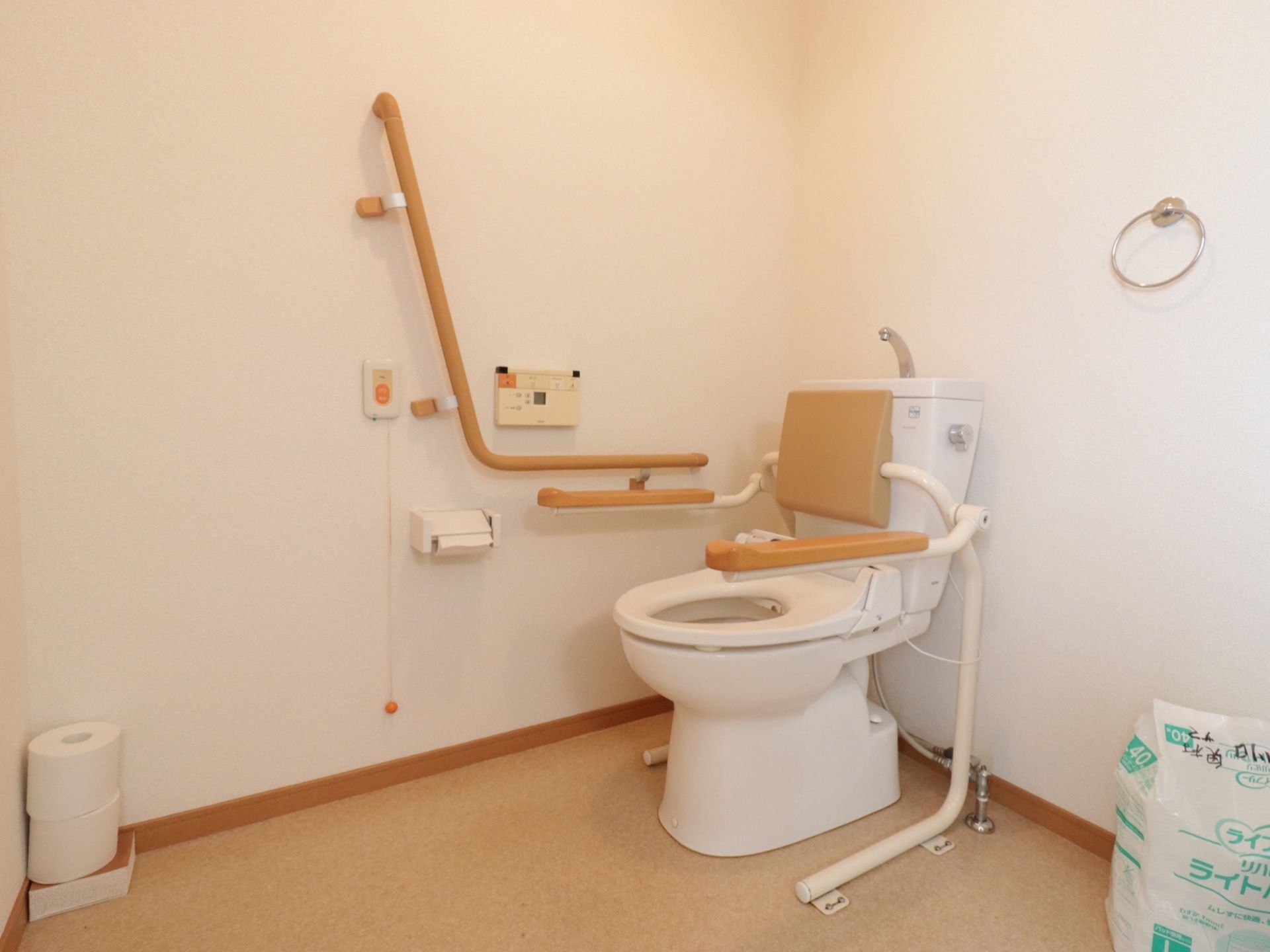 トイレの便座には背もたれと、両脇に跳ね上げ式の手すりが備わっている。壁にもしっかりとした手すりと呼出ボタンが付いている。