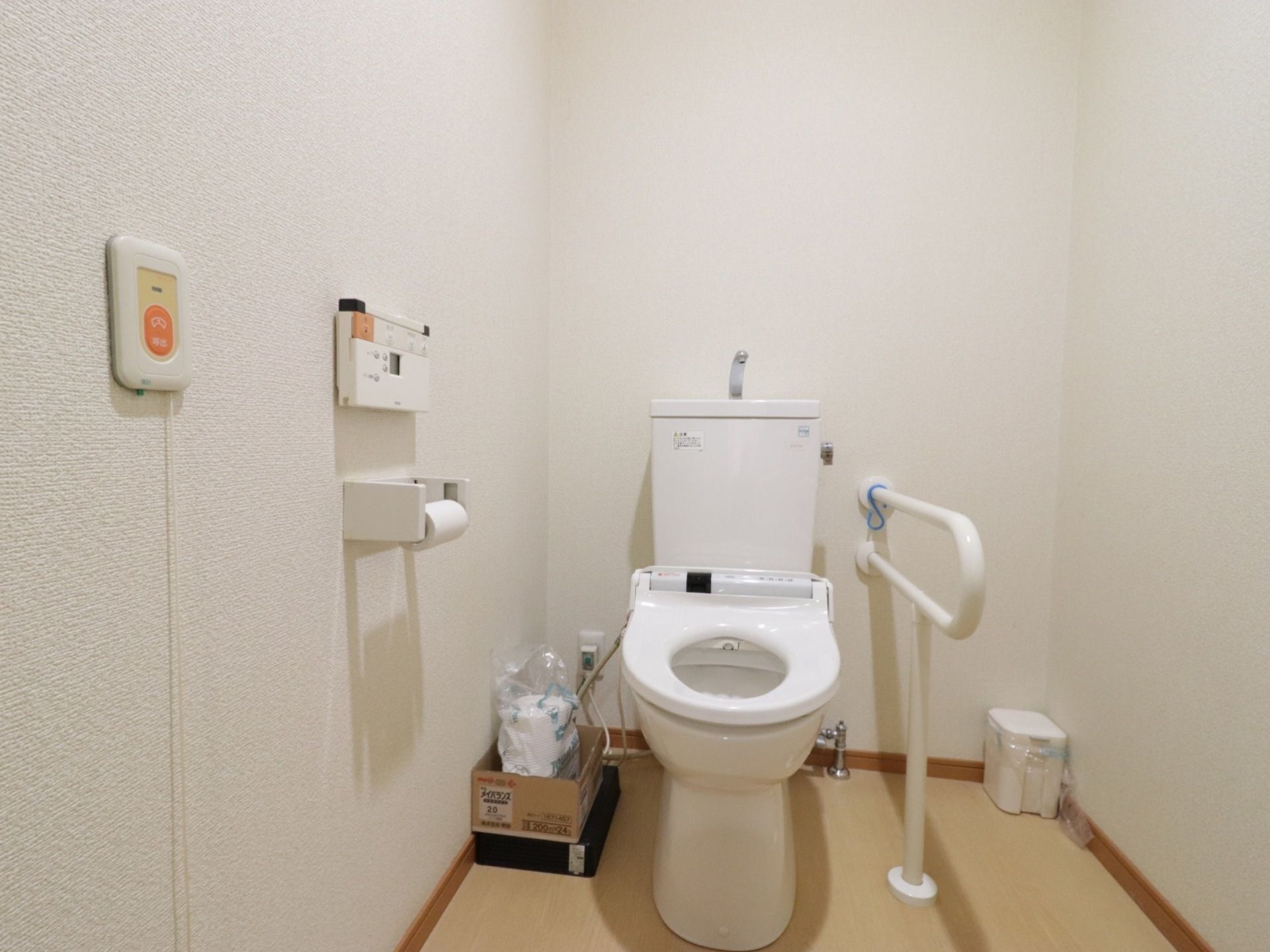 白壁のトイレは明るく清潔感がある。便座脇には足腰の負担を減らしてくれる手すりが設置されている。壁には呼出ボタンも付いている。