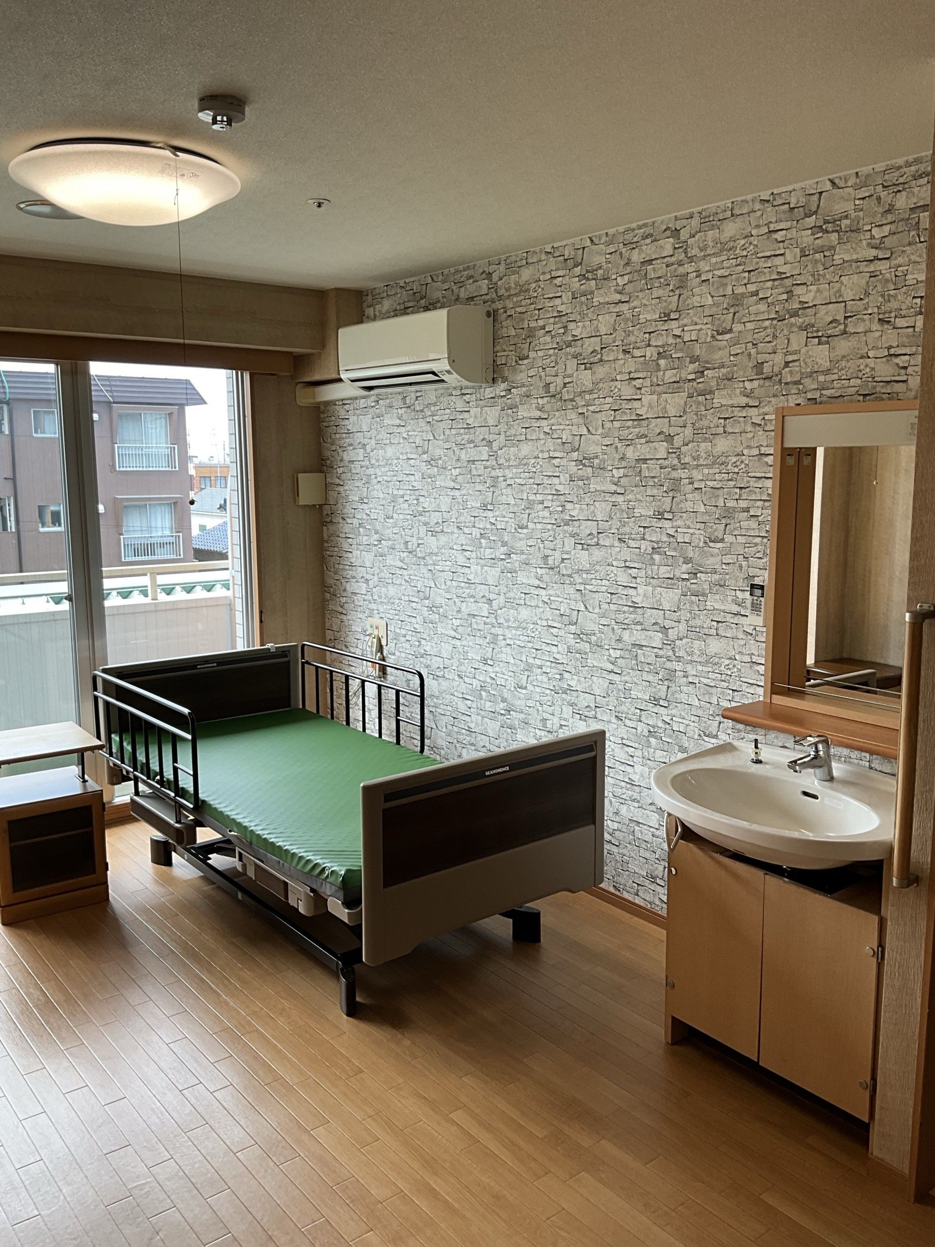 部屋には、キャビネットやサイドテーブルを配置して、住みやすい環境にできる。ベッドに黒い柵を設置して、転倒防止対策をしている。