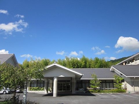 奥に背の高い樹木がたくさん生えている、グレーの屋根の施設
