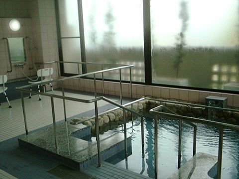 大きな窓から外光が差しこむ浴室には、数人で入れる大きな浴槽がある。浴槽を囲むように手すりが設置されている。洗い場も複数備わっている。