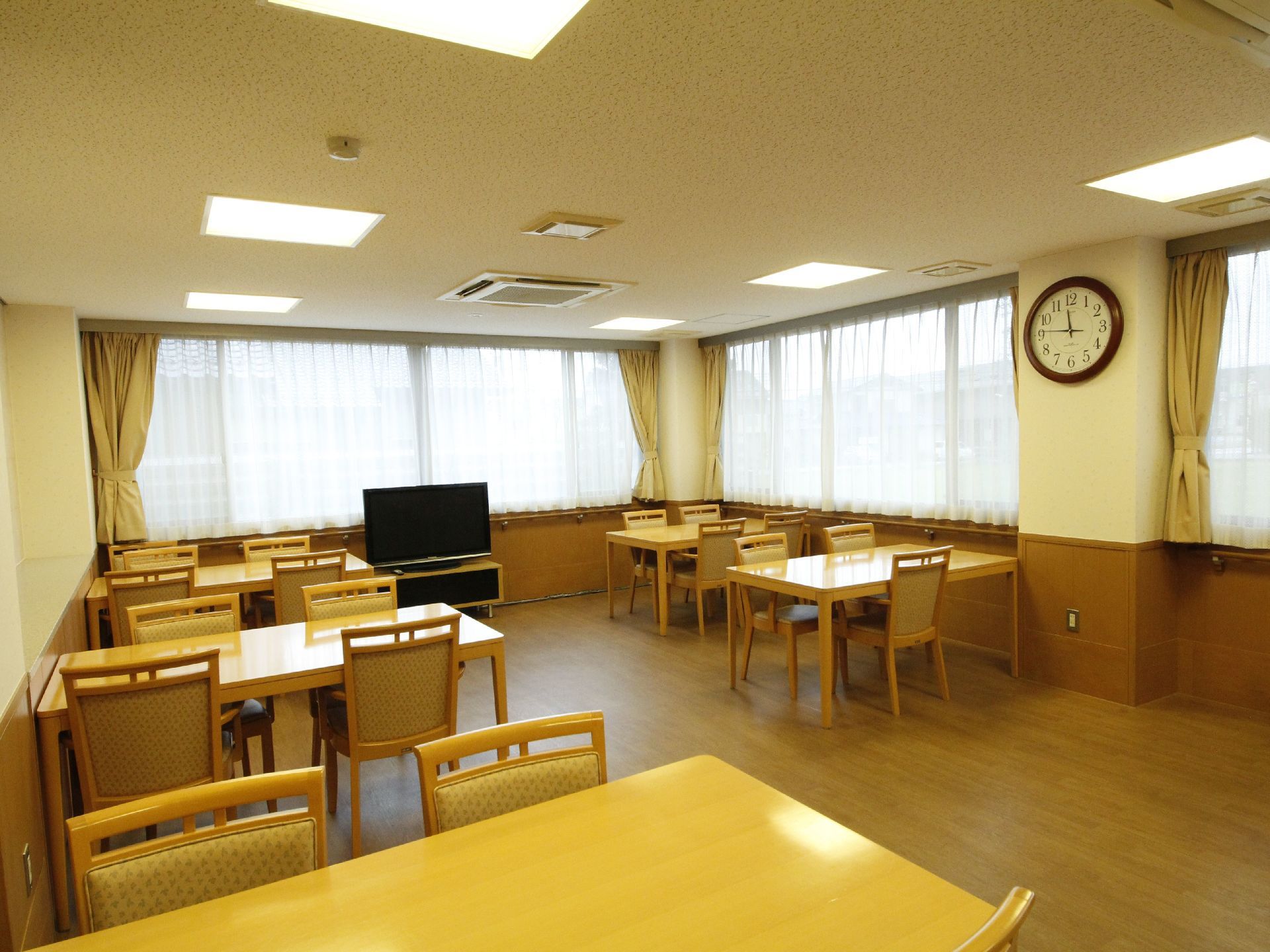 大きな窓がある広々とした明るい食堂。大型のテレビが設置されている。天井には埋込式の空調が取り付けられている。