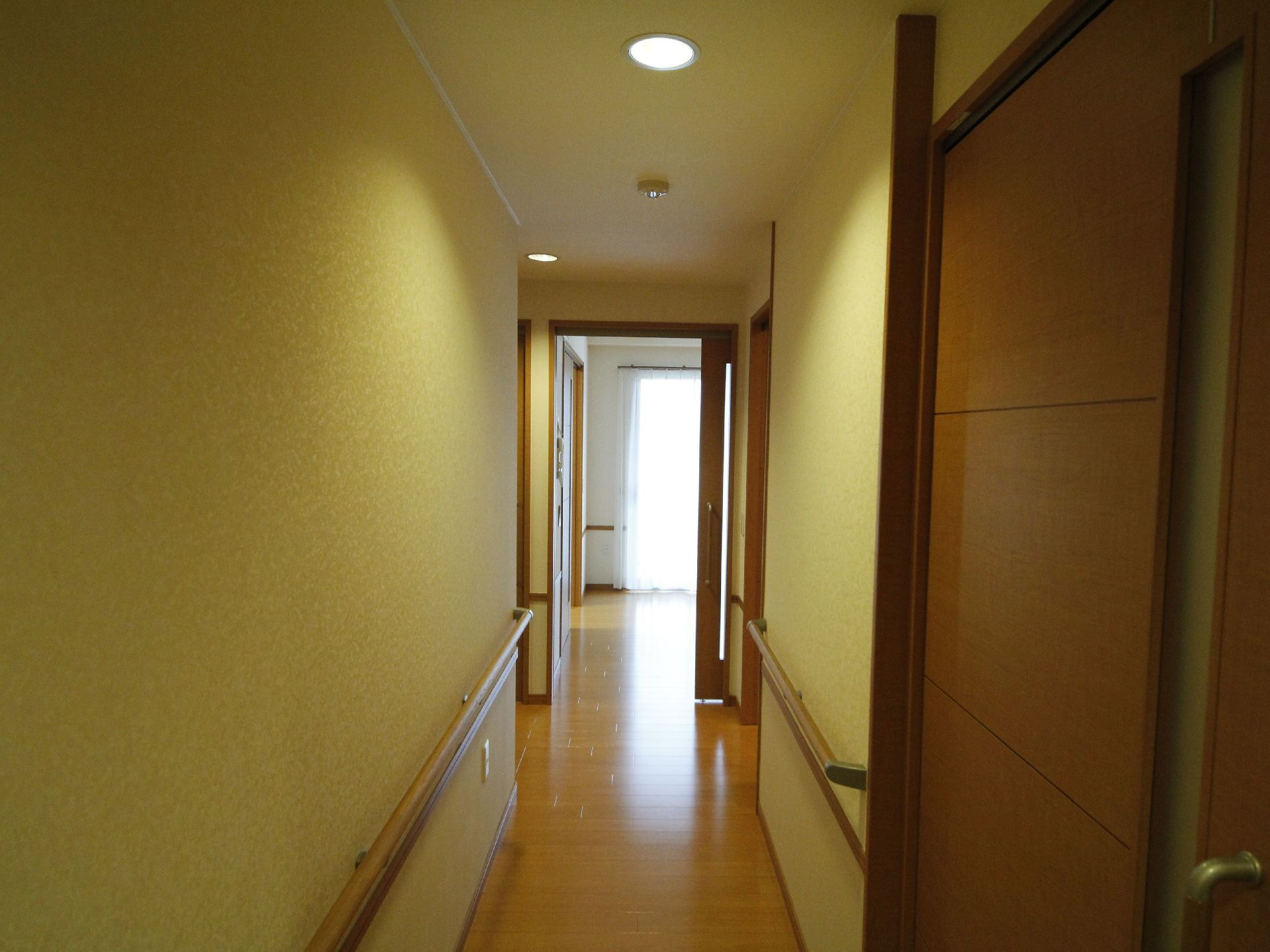 居室内の廊下の写真。床はフローリングになっている。壁には手すりが付いている。左右に複数の扉が並んでいる。