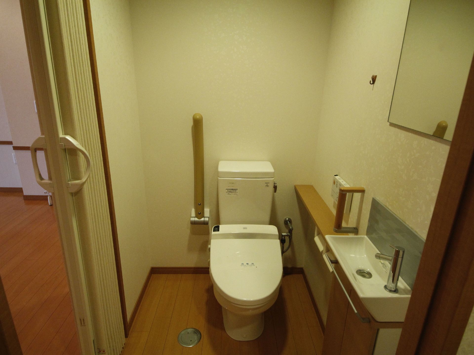 トイレは洋式トイレが置かれている。横には可動式のひじ掛けが取り付けられている。入口はアコーディオンカーテンが付いている。