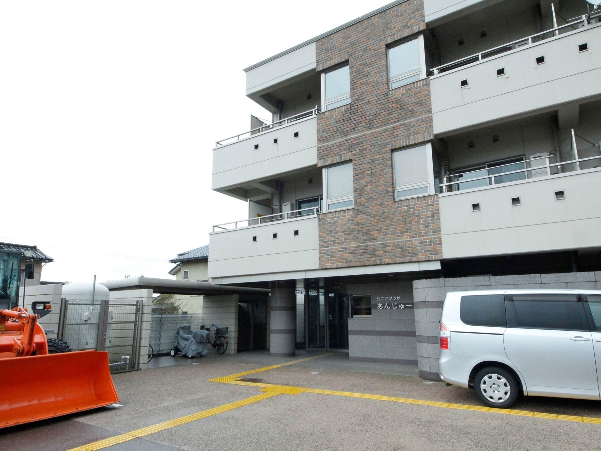 建物の前には車が１台停まっている。屋根が付いた駐輪場がある。入口まで黄色の点字ブロックが繋がっている。