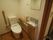 白色と明るい茶色を基調とした洋式のトイレである。可動式の手すりや手洗い場が備わっている。壁にはフックが取り付けられている。
