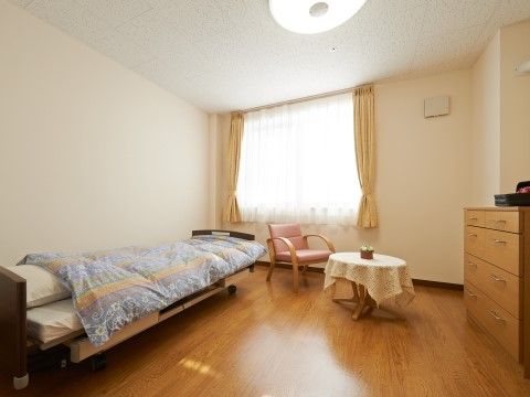 右手の壁際に木製のチェストが置かれている、照明が点いた居室