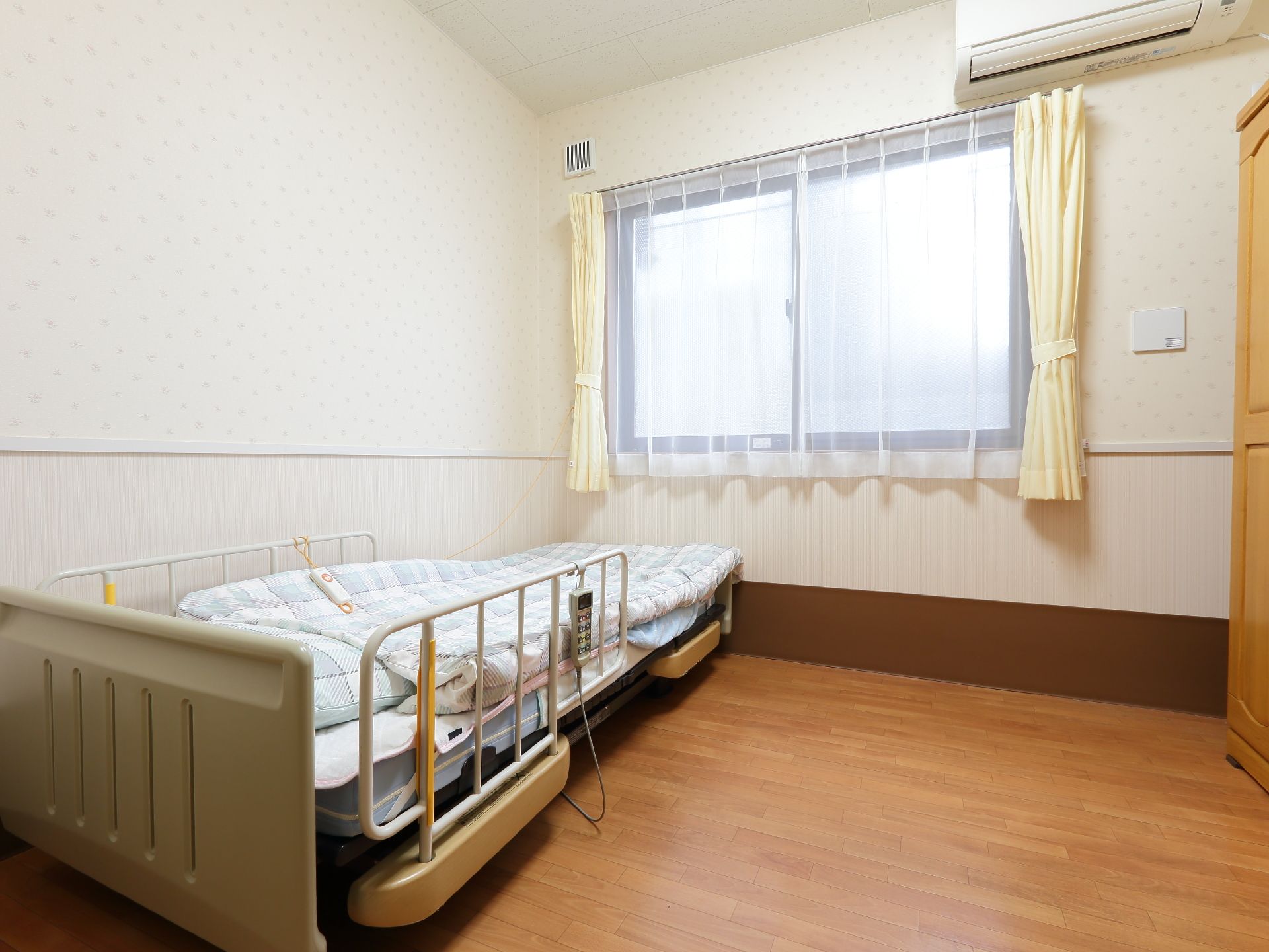 薄手のカーテンが掛けられている窓の前に置かれたベッド