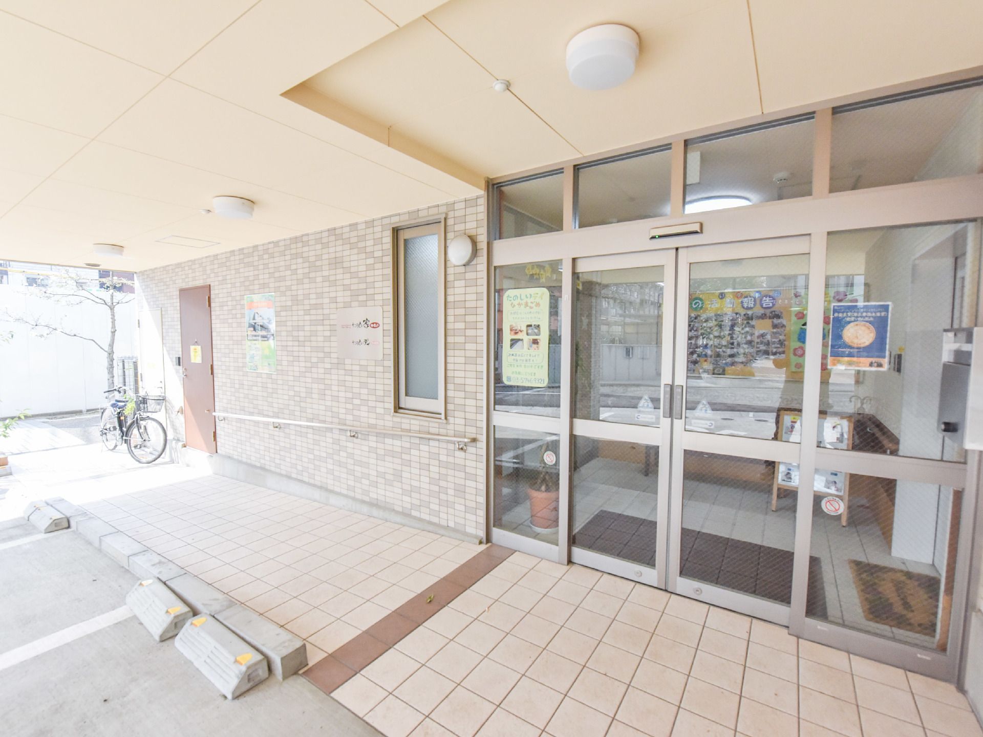 エントランスの左側には職員用の玄関と車いす用のスロープがある。その壁に沿って手すりが備え付けられている。