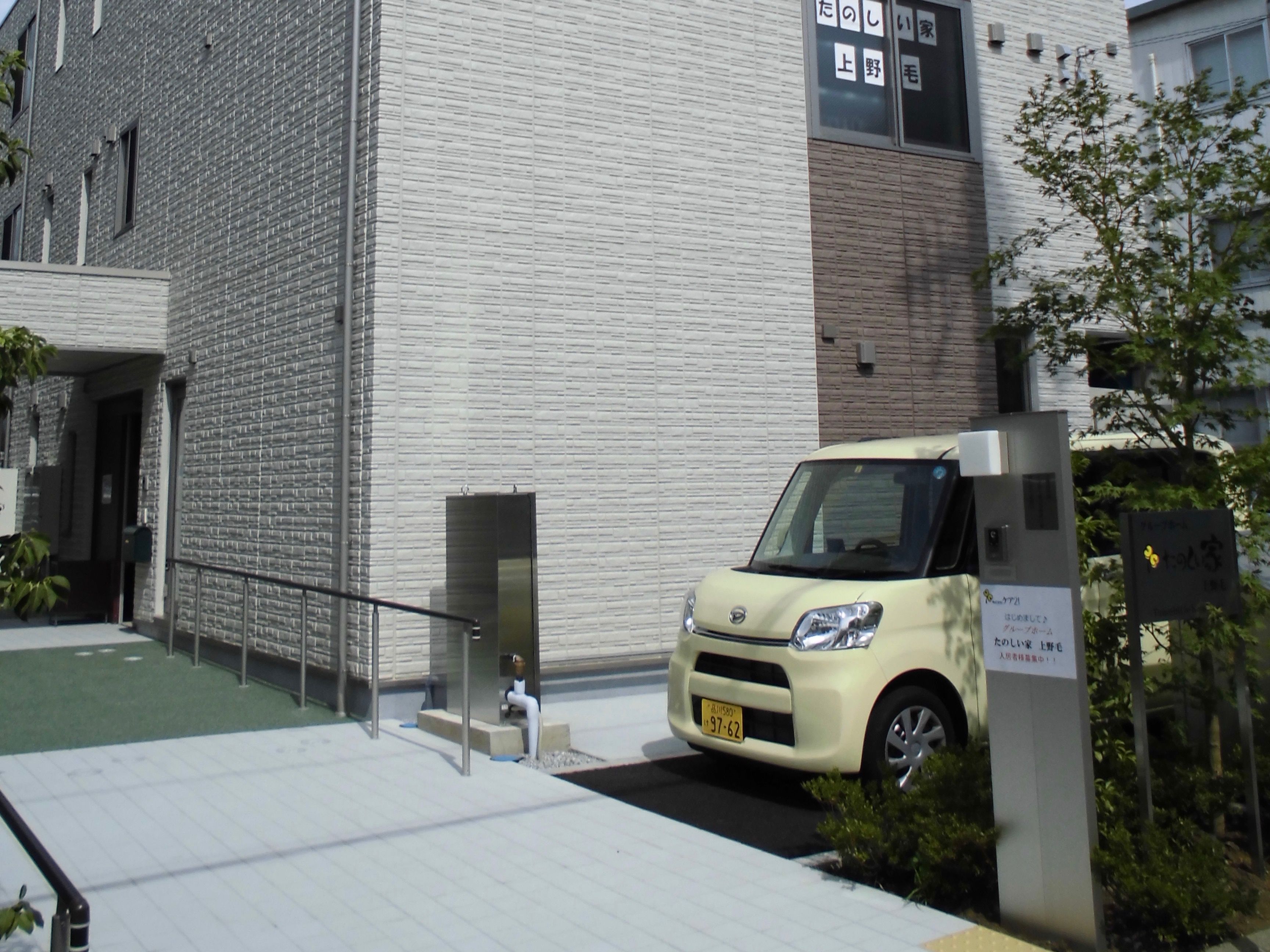 駐車場にクリーム色の軽自動車が停まっている施設の玄関前