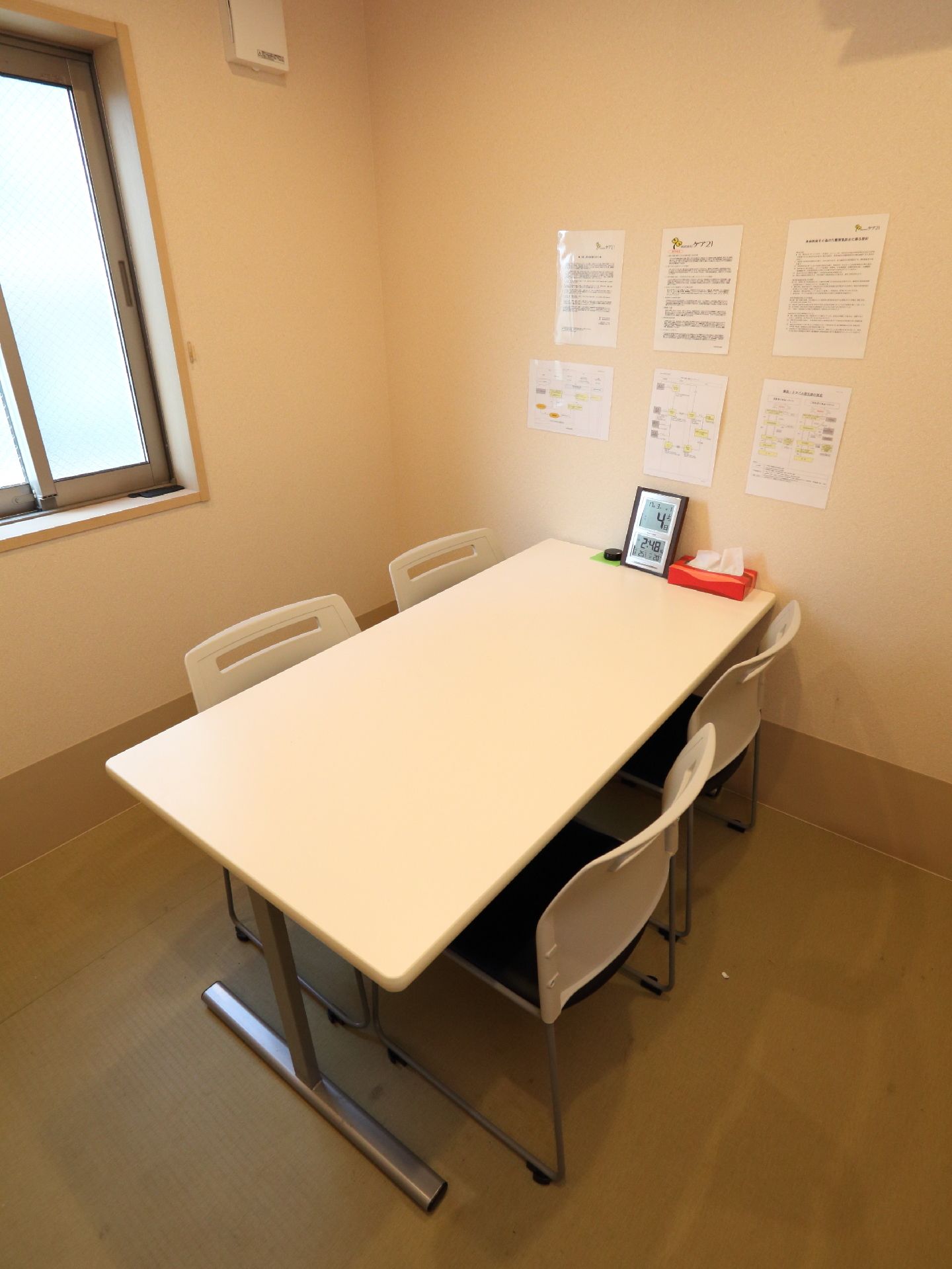 陽の光が差し込む白で統一された部屋。机と椅子があり、ミーティング等ができる。壁には連絡事項等が貼られている。