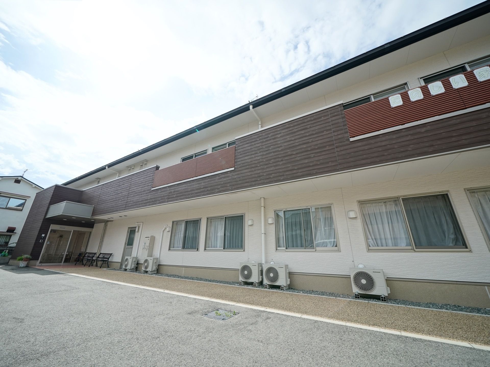 ２階建ての広い建物で、玄関は自動ドアになっている。窓とバルコニーが設置されており、外壁に施設の名前が書かれた看板が貼られている。