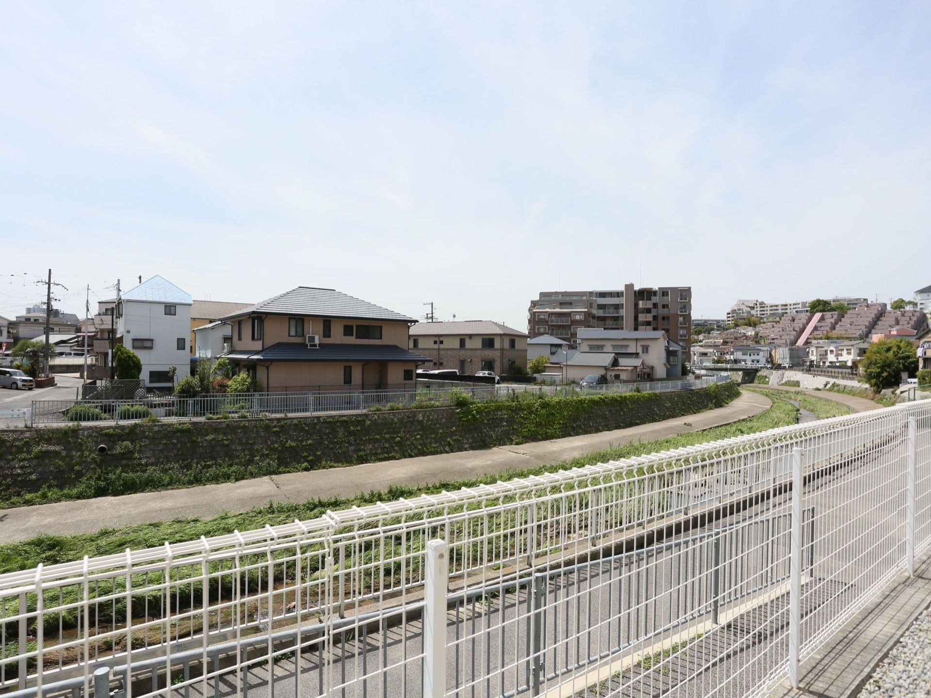 フェンスの内側から川辺の道と住宅街が見える。見晴らしがいい。また、フェンスの外側には道路へ出るためのスロープがある。