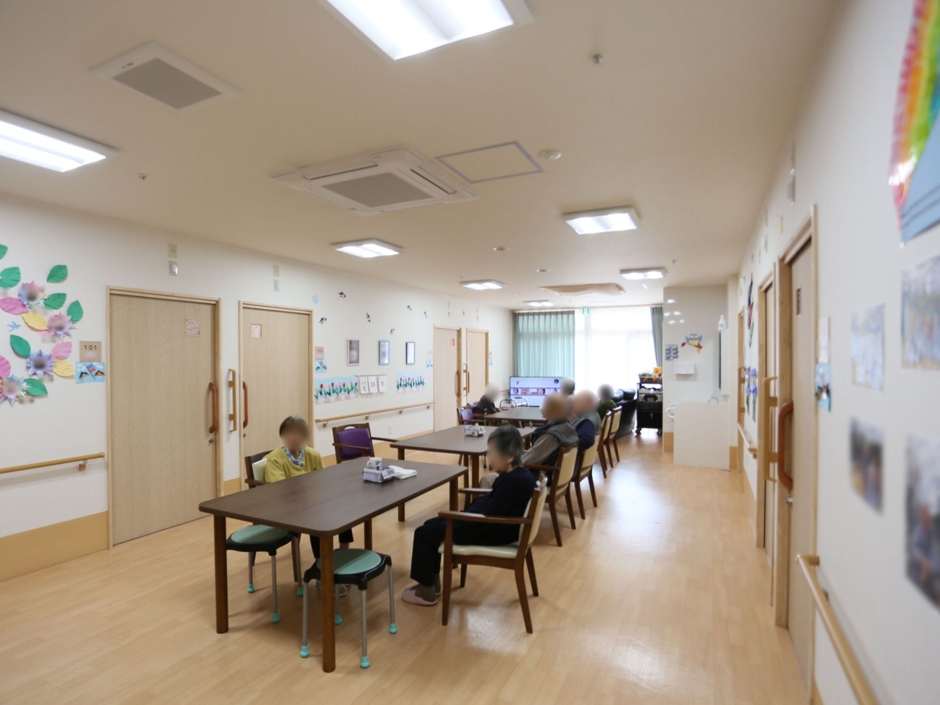 広々とした空間に複数の机と椅子が置かれている。奥には大きな窓があり、そのわきにはテレビが置かれている。