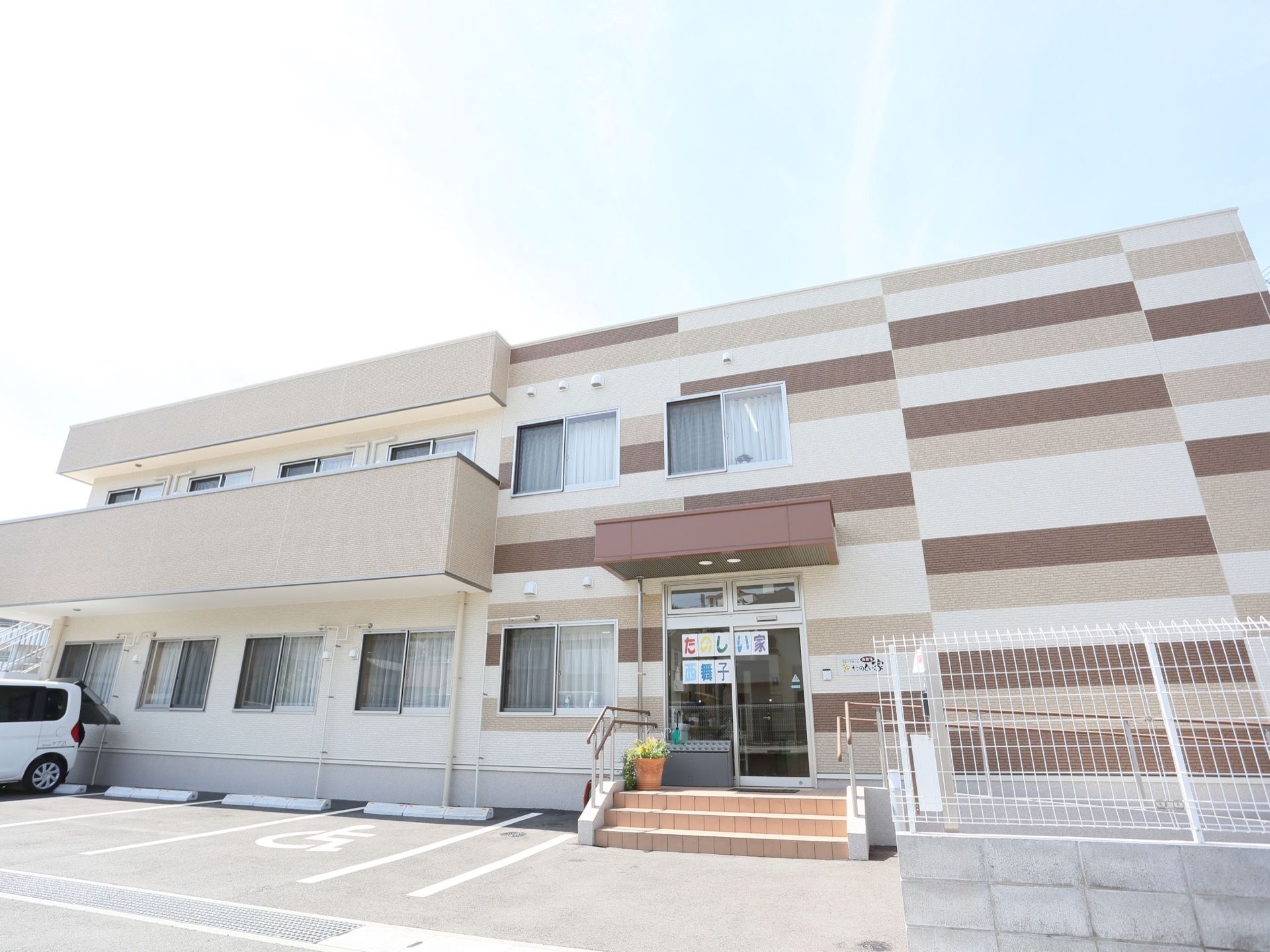 建物の手前側には複数の駐車スペースがある。建物は半分がデザイン性のある色彩で、もう半分が明るい色彩でまとめられている。