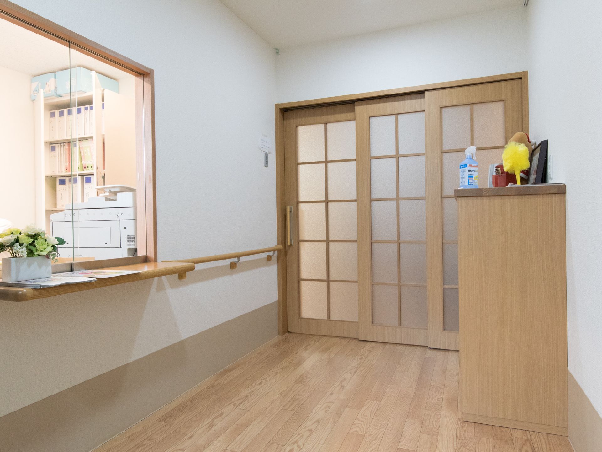 事務室では、コピー機や書類の入ったフォルダーを並べた棚などが置かれている。ガラス戸になっているので、廊下から事務室がみえる。