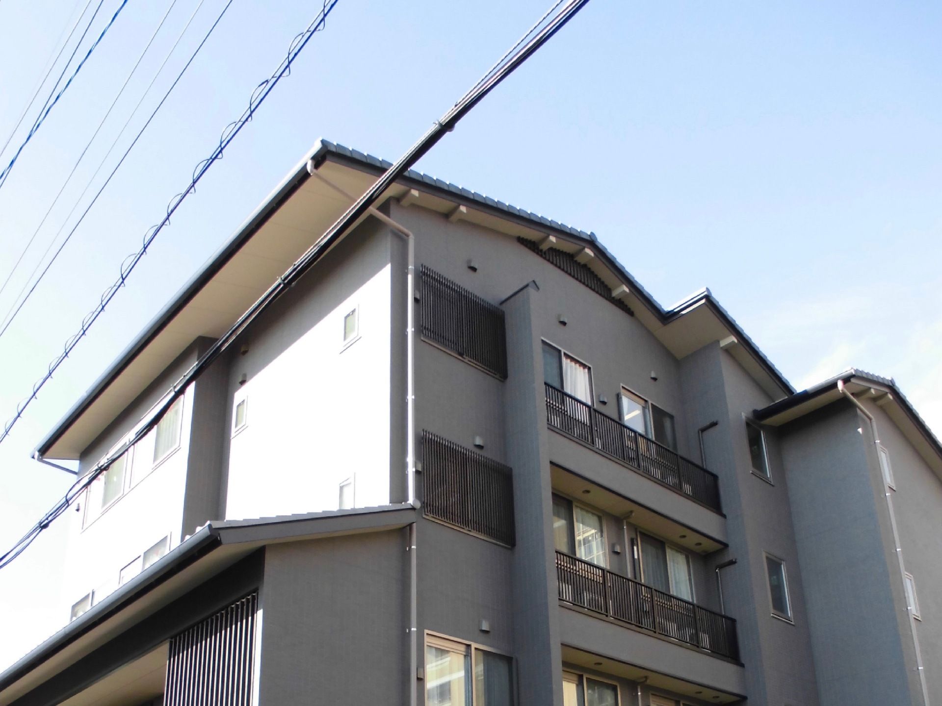 瓦屋根になっている、外壁をグレーで統一した３階建ての建物