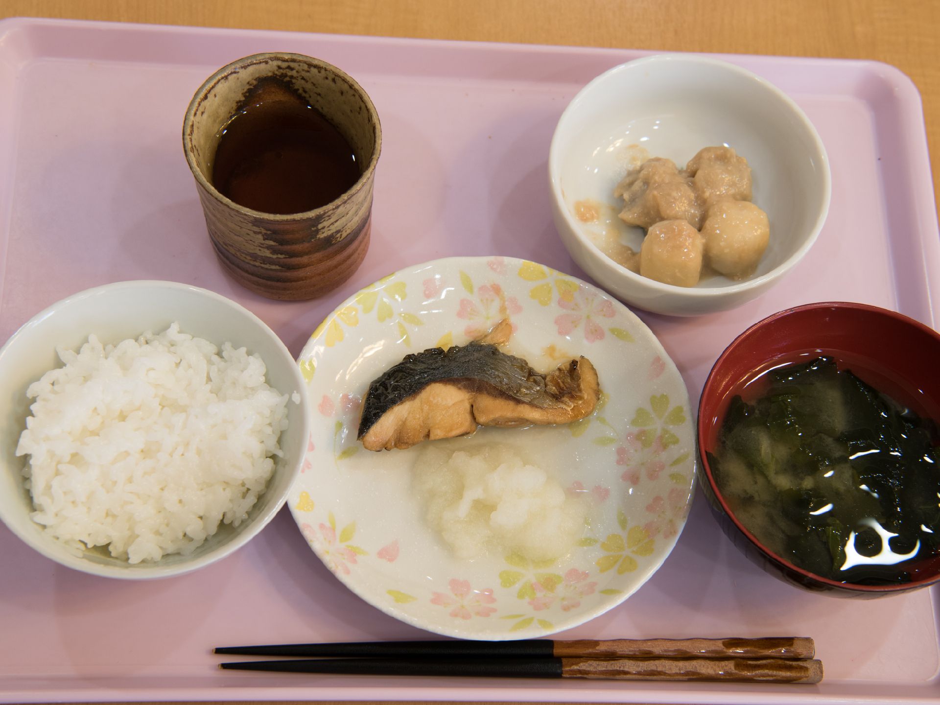 左側にはご飯が置かれている。中央にはおかずがある。右側には味噌汁が置かれている。右上には副菜がある。下には箸が置かれている。
