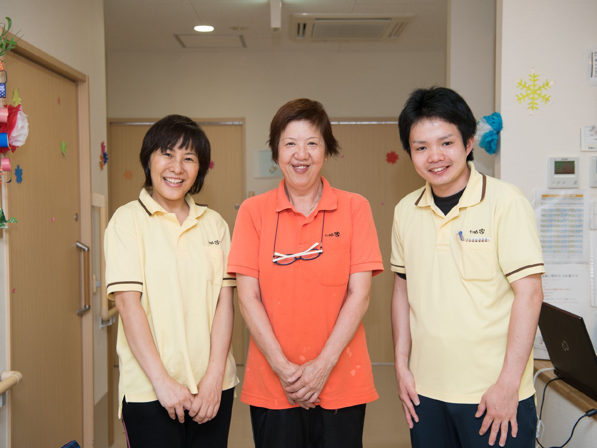 壁やドアに折り紙の飾り付けがされた廊下で笑っているスタッフ