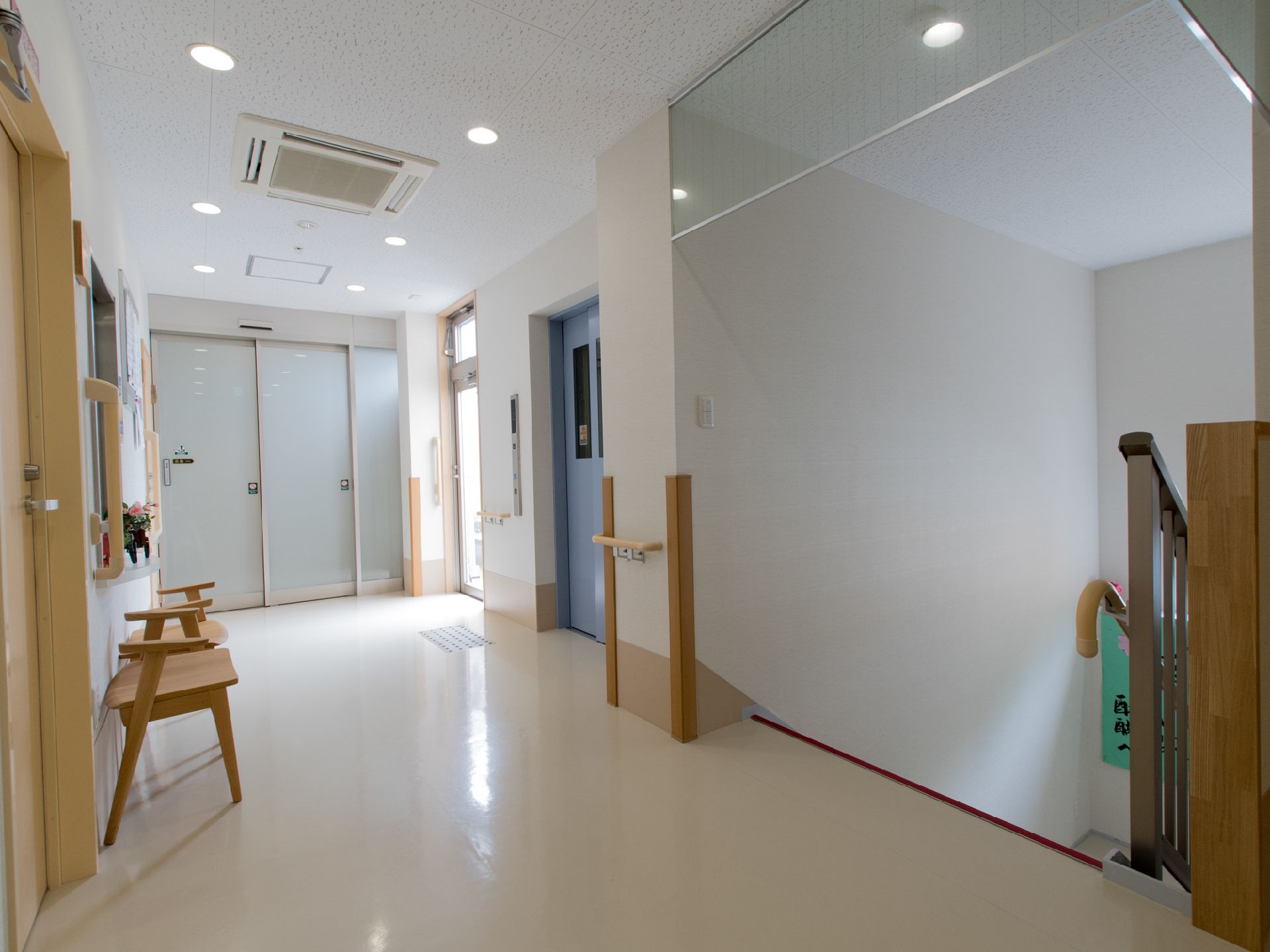 右側には下りの階段があり、その奥にはエレベーターがある。左側には椅子が2脚置かれている。天井にはエアコンが付いている。