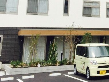 黄色い軽乗用車が停まった駐車場とその奥に建っている施設