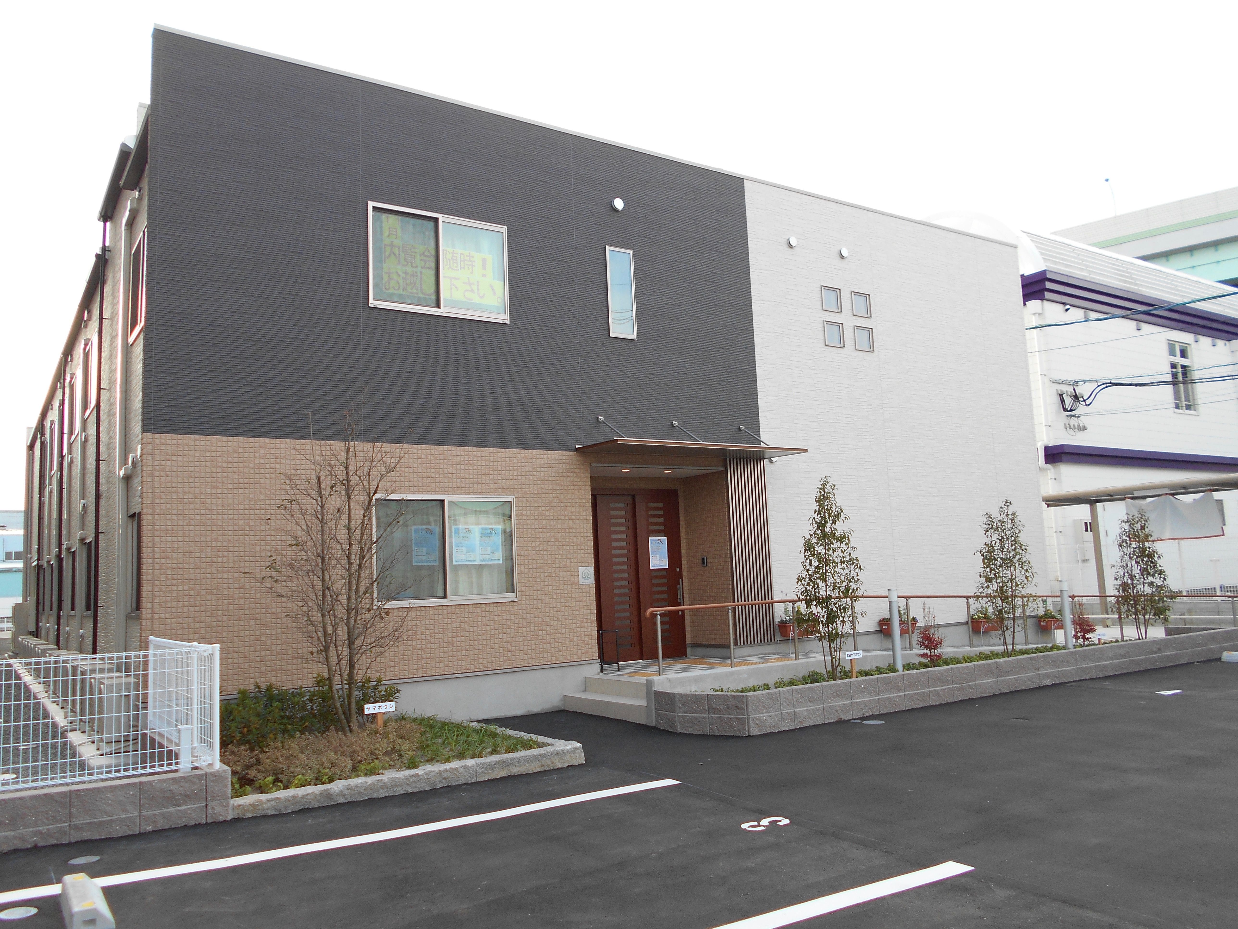 内覧会の広告が２階の窓に貼りだされている、グレーと白、ベージュの建物