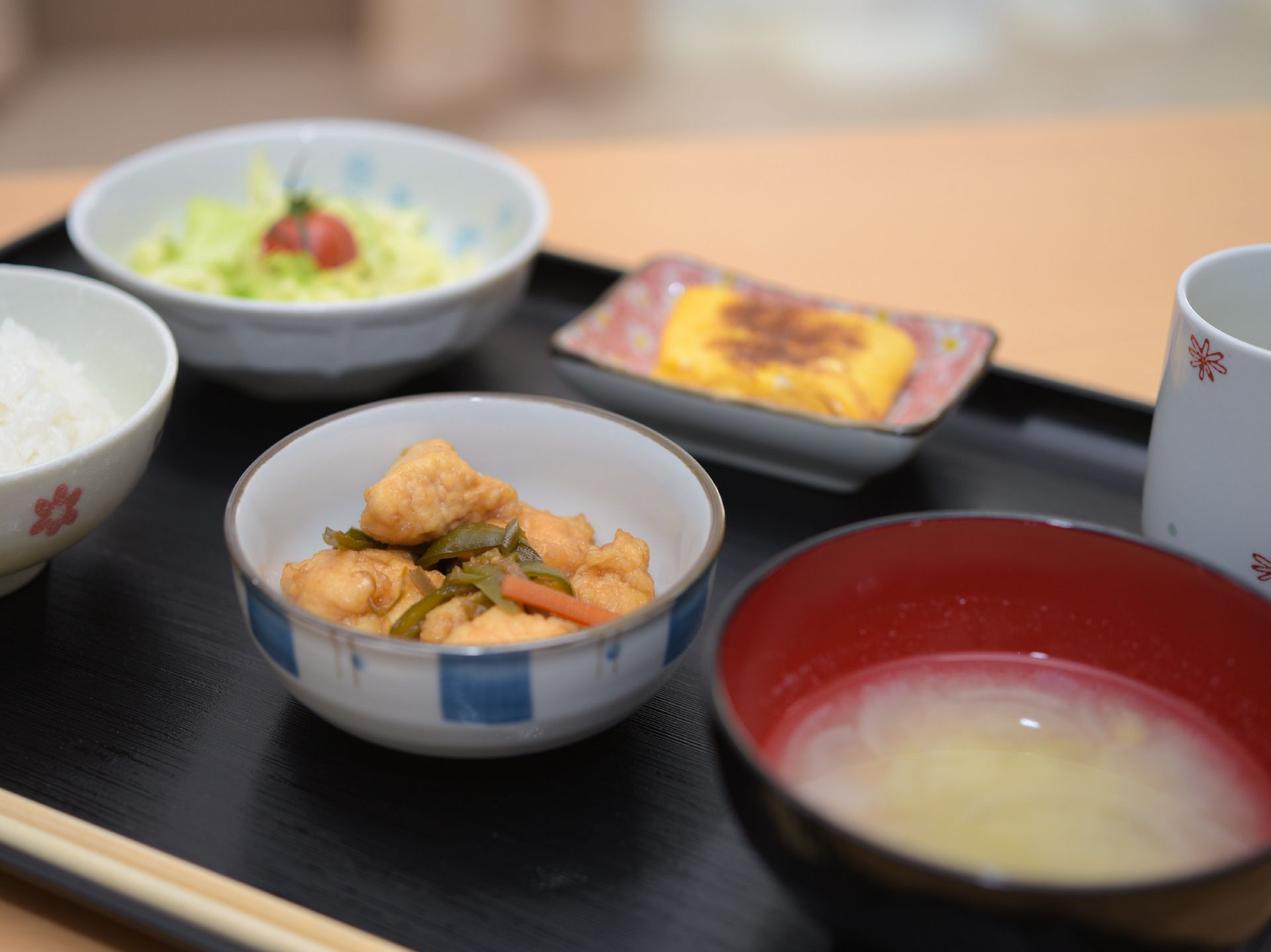 卵焼きやサラダ、かんもの煮物が配膳されている黒いトレイ