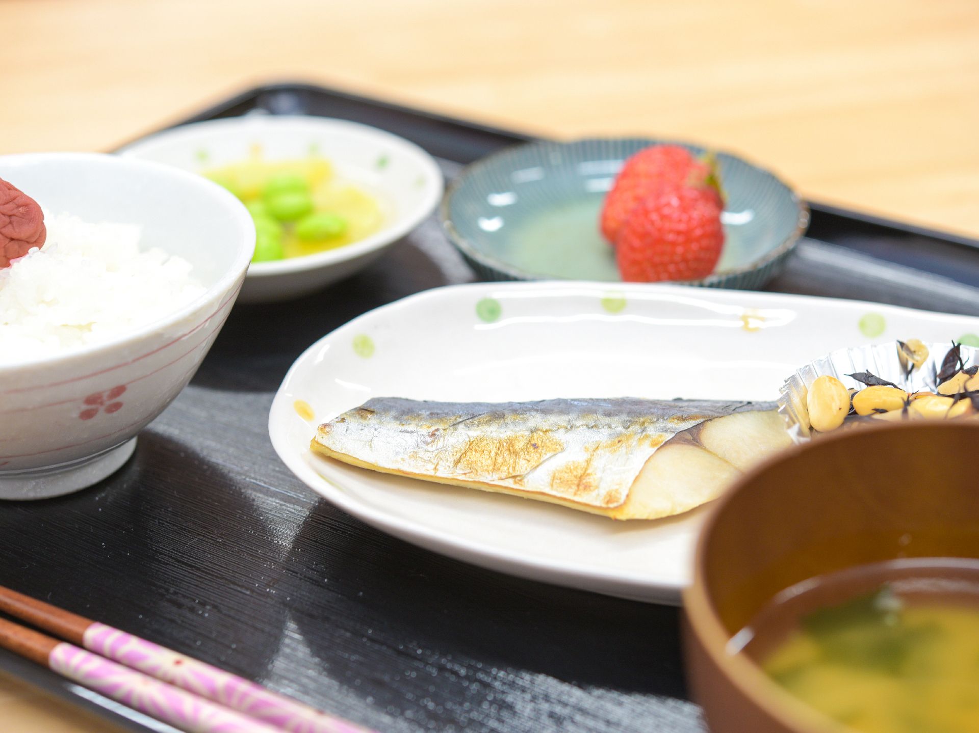 焼き魚をメインに、煮豆や季節の果物などがトレイに乗っている食事