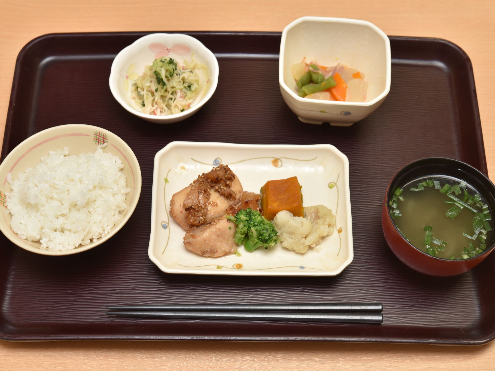 お膳の上にはご飯と味噌汁、その間には長方形の皿がありおかずが盛られている。さらに円形と正方形の小鉢があり、それぞれにおかずが用意されている。