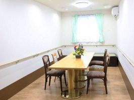 壁には切れ目なく手すりが設置されている。部屋の中央に長テーブルがあり、椅子が並べられている。テーブルの上には花が飾られている。