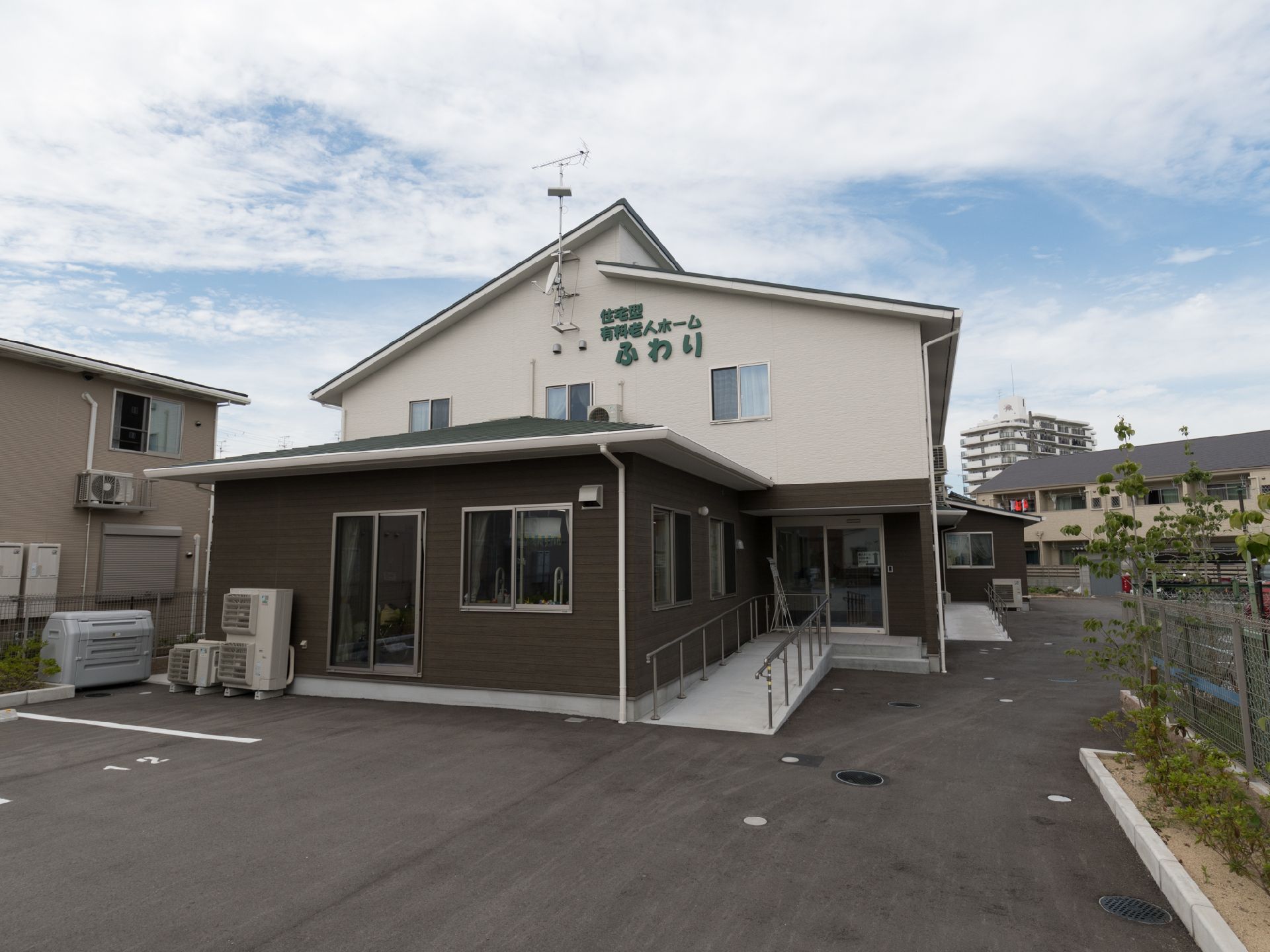 駐車場は広く、施設の外壁は茶色と白色のツートーンになっている。2階部分に緑色で施設名が書かれている。