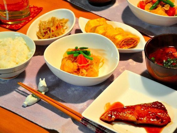 ランチョンマットの上にご飯や卵焼き、汁物、きんぴら、魚の照り焼き、ジャガイモの煮つけが乗っている。コップの下にはコースターが敷いてある。