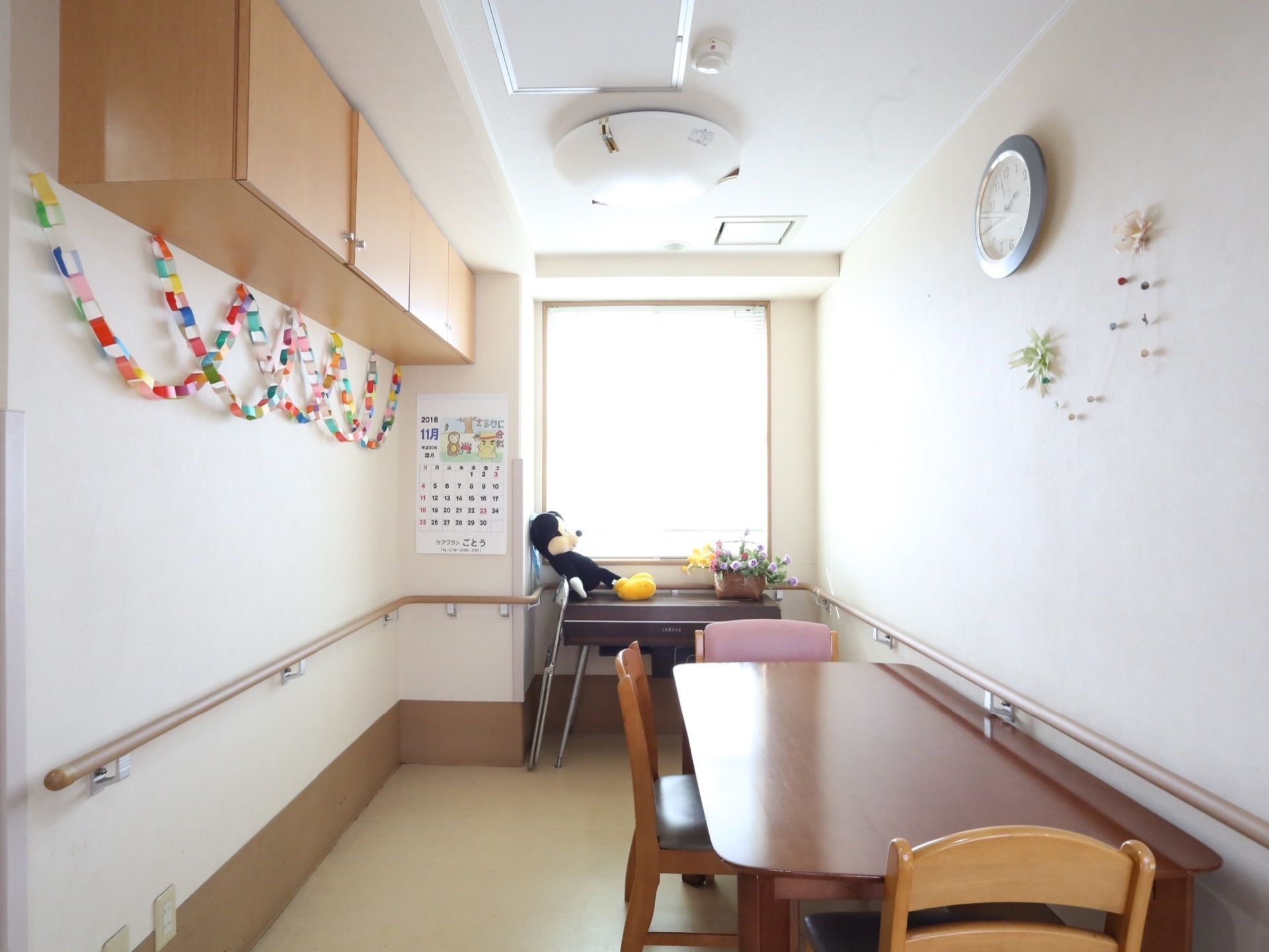 窓がある半個室の空間にテーブルが置かれ椅子が備えられている。白色の壁には淡い茶色の木目の手すりが取りつけられている。