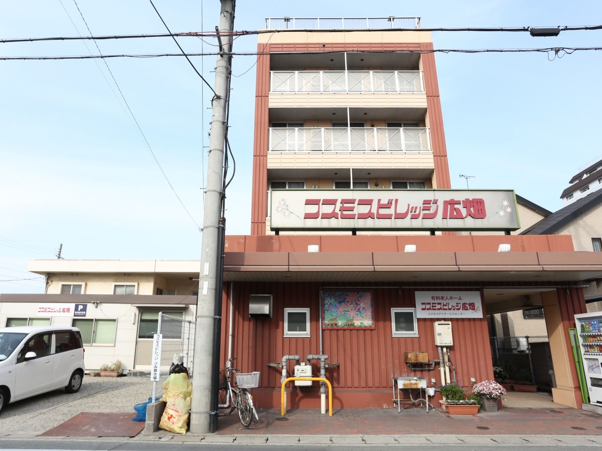 道路側から通路を進んだところに入口がある。建物の前面にベランダがあり、一階の屋根に大きな文字で施設名が記してある。