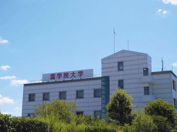 私立大学のキャンパス建物である。建物は明るい色で、屋上に看板が掲げられており、前面には緑が茂っている。