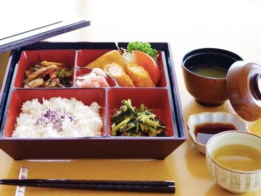 お弁当箱の中に、ご飯、揚げ物、野菜、添え物が２種類と漬物が入っている。味噌汁、醤油皿、お茶と箸が添えられている。