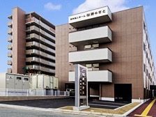 建物の前に大きな看板が立っている、４階建ての茶色と白の建物