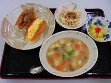黒に赤い縁取りのトレイの上にシチュー、ホットドッグ、小鉢、デザートが並べられている。ホットドッグは卵サラダと野菜の２種類がある。