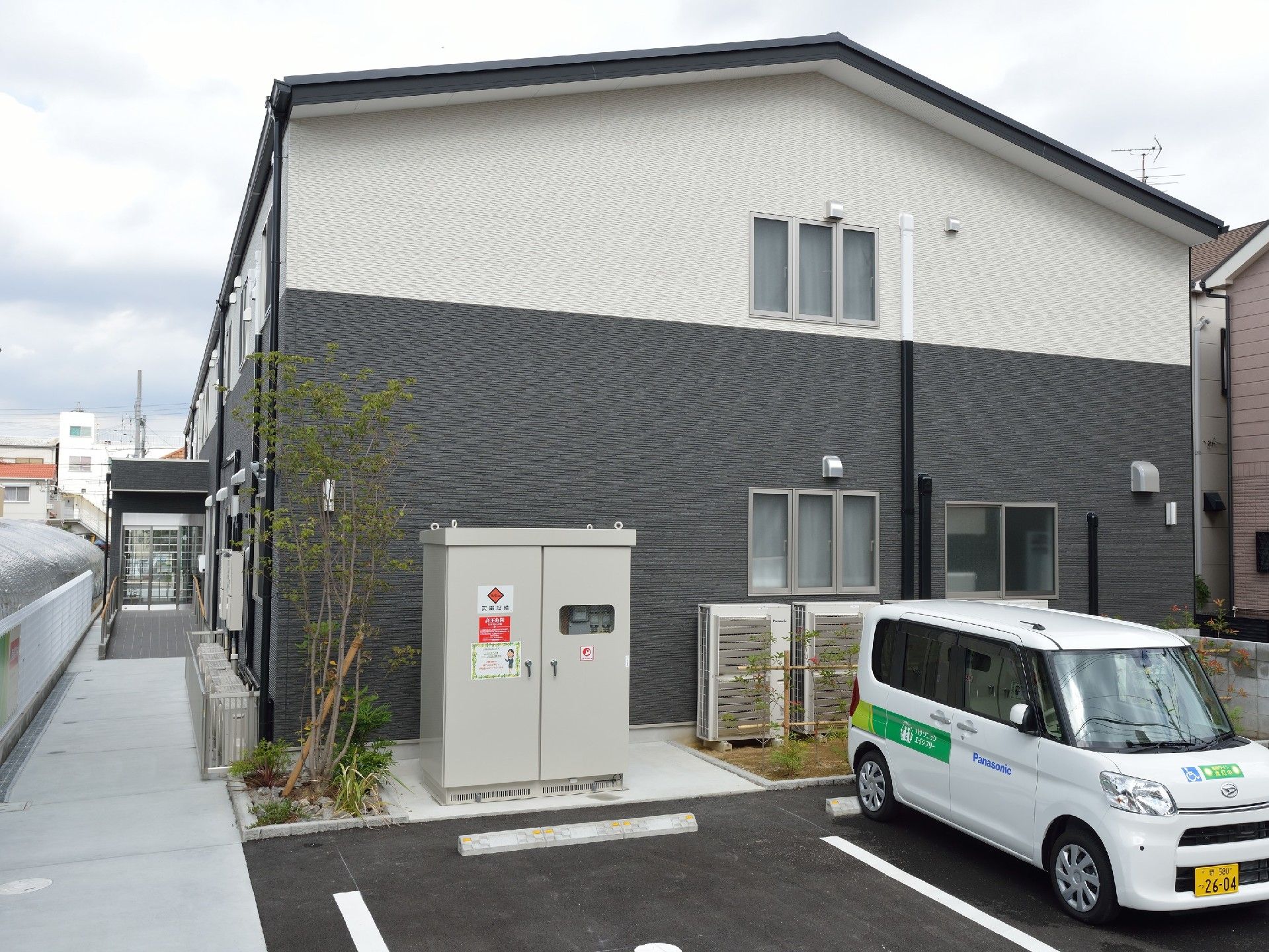 駐車スペースがある２階建ての建物には玄関には手すり付きのスロープも付き、周辺には木も植えられている。