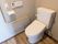 白を基調とした清潔感のあるトイレである。壁には、L字型の手すりを取付けられており、タンクのあるトイレとなっている。