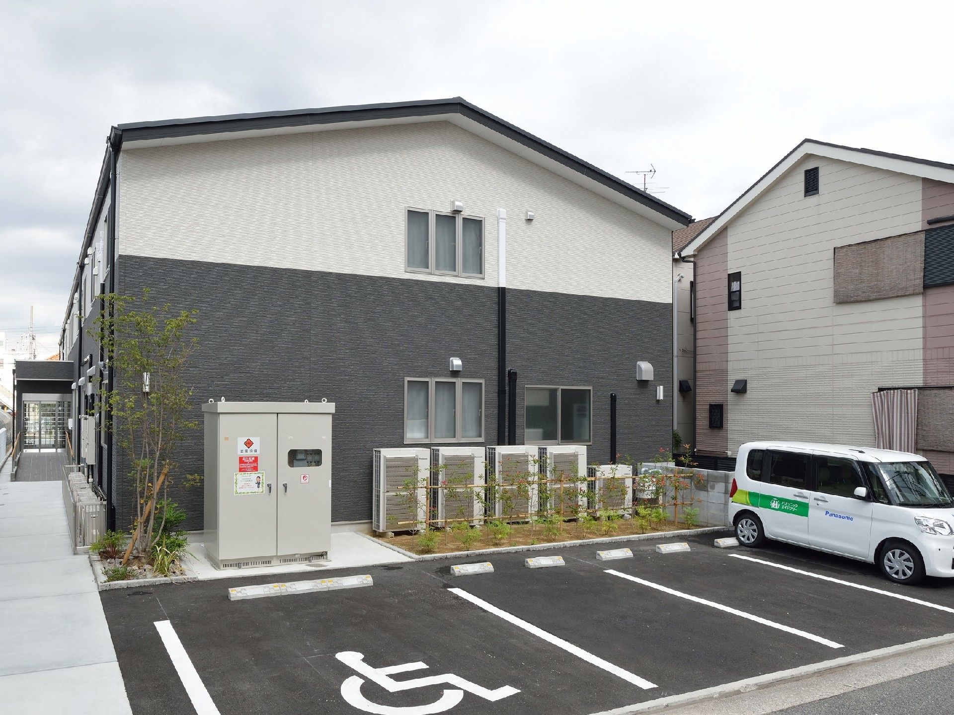 ダークグレーと白の2階建ての建物。建物周辺には木が植えられ、駐車場も完備されている。