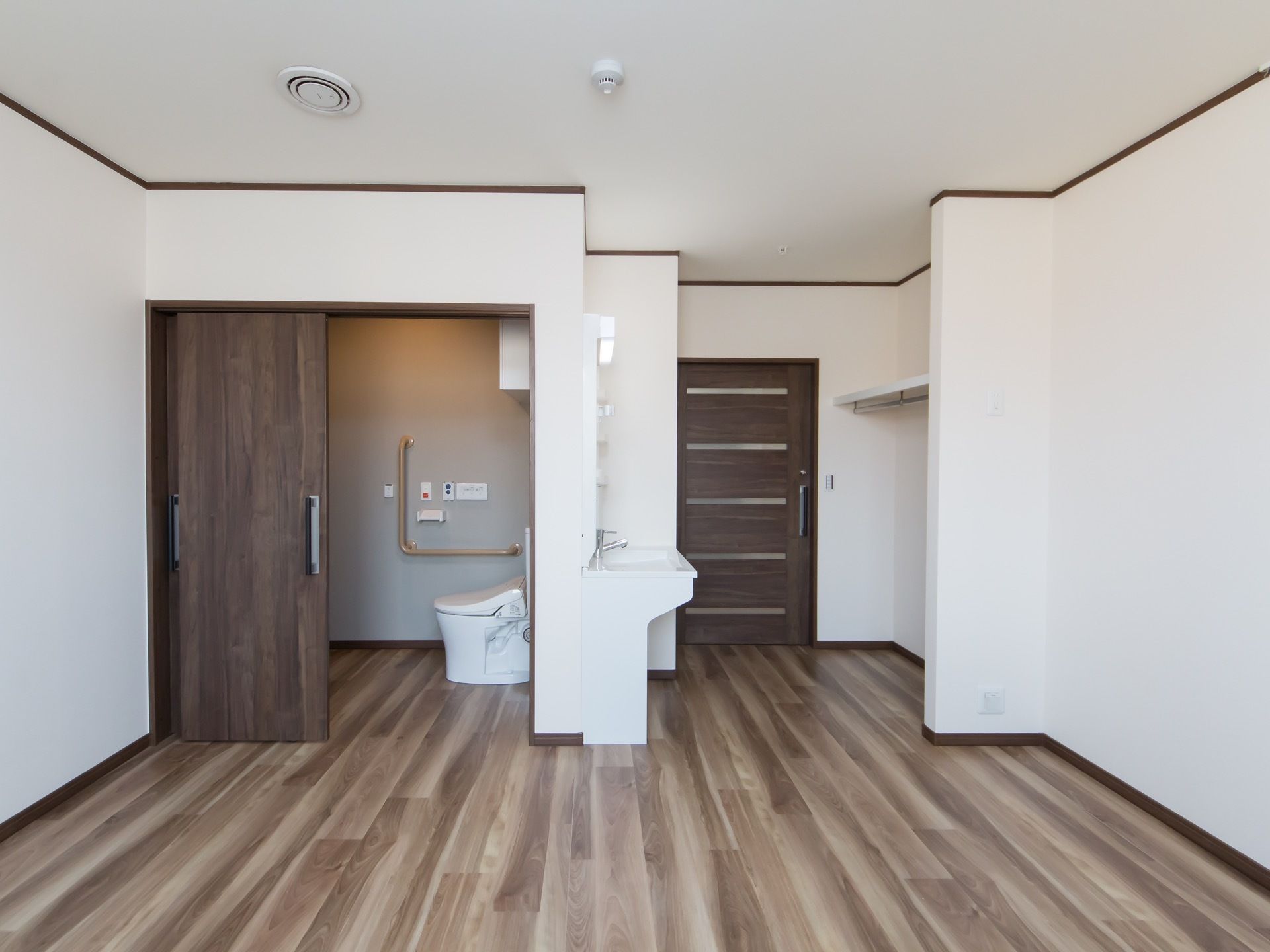 白い壁と焦げ茶のドアで、落ち着いた雰囲気の居室となっている。トイレの扉は、引き戸式になっており、トイレ内の壁には手すりがついている。