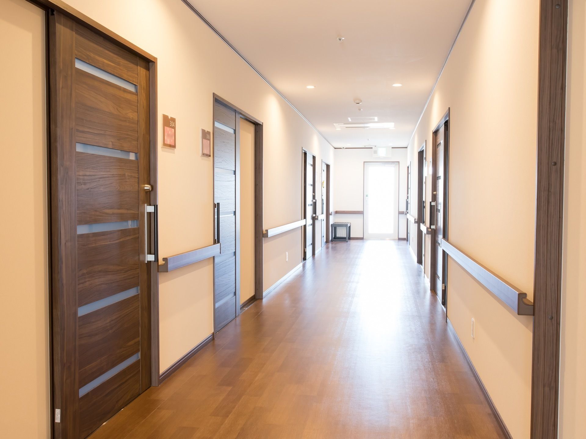 通路はフローリングで、まっすぐに続いている。部屋の扉が並んでおり、壁には手すりが備え付けられている。