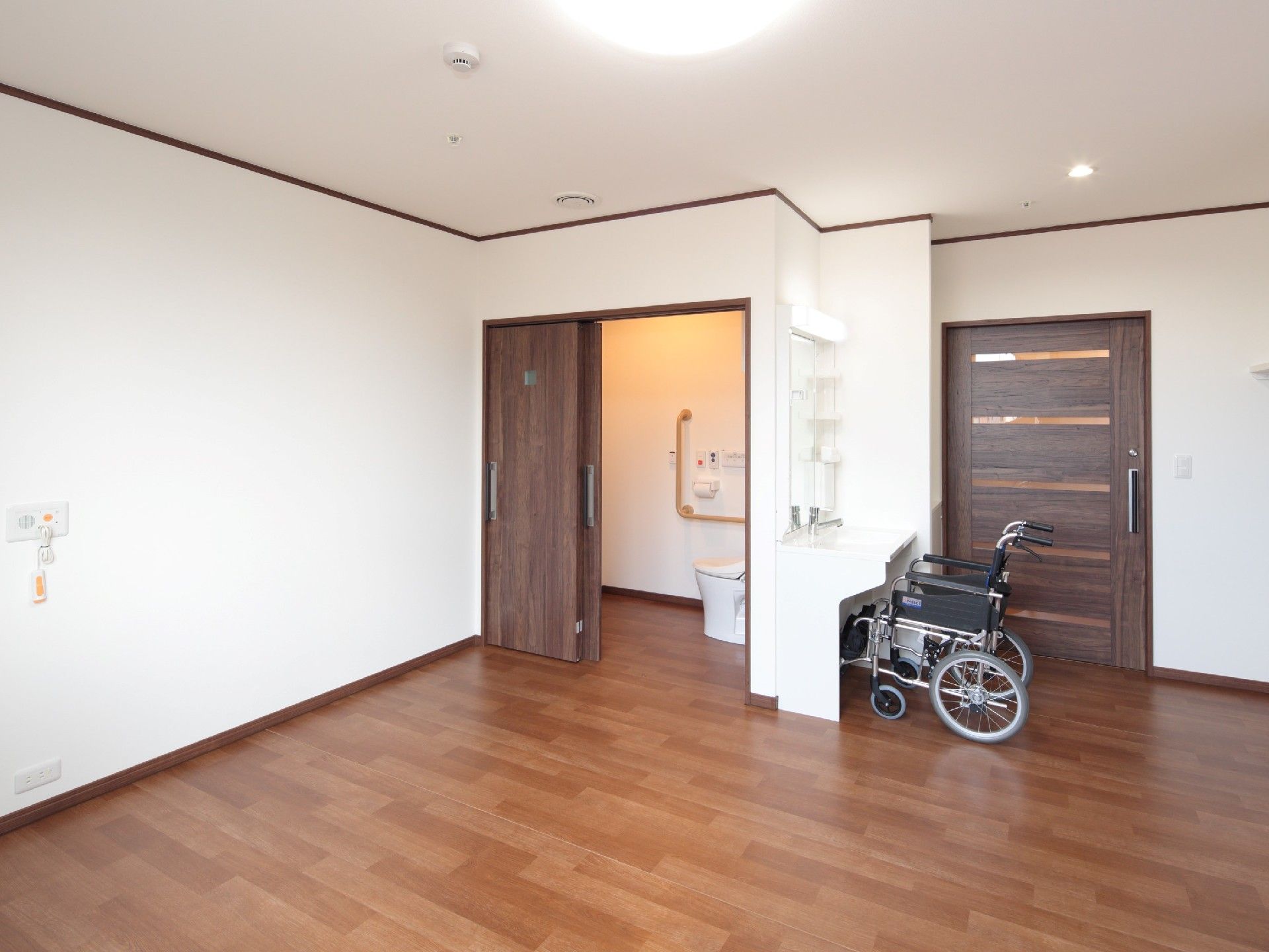 フローリングのシンプルな居室。トイレや洗面所、緊急通報装置が付いている。