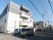 施設は住宅街に建てられている。白色とグレー色の3階建ての建物である。敷地内には駐車場があり、複数の車が停められている。