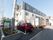 3階建ての白い壁面の建物がある。3階部分のみがグレーの壁になっている。建物の側には、舗装された駐車場がある。