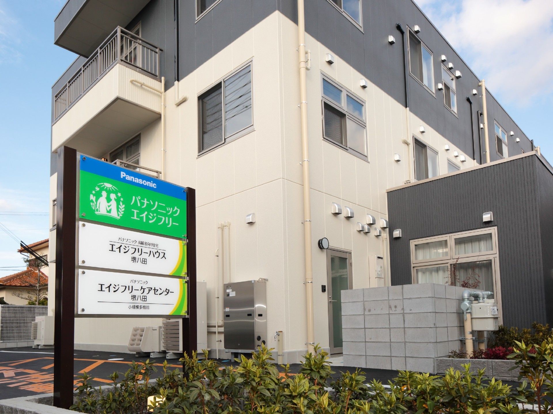 3階建ての建物にはベランダが付き、玄関の周りには木や花も植えられ、駐車スペースもある。